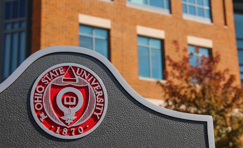 Picture of the seal of The Ohio State University on a sign with a brick building in the background.